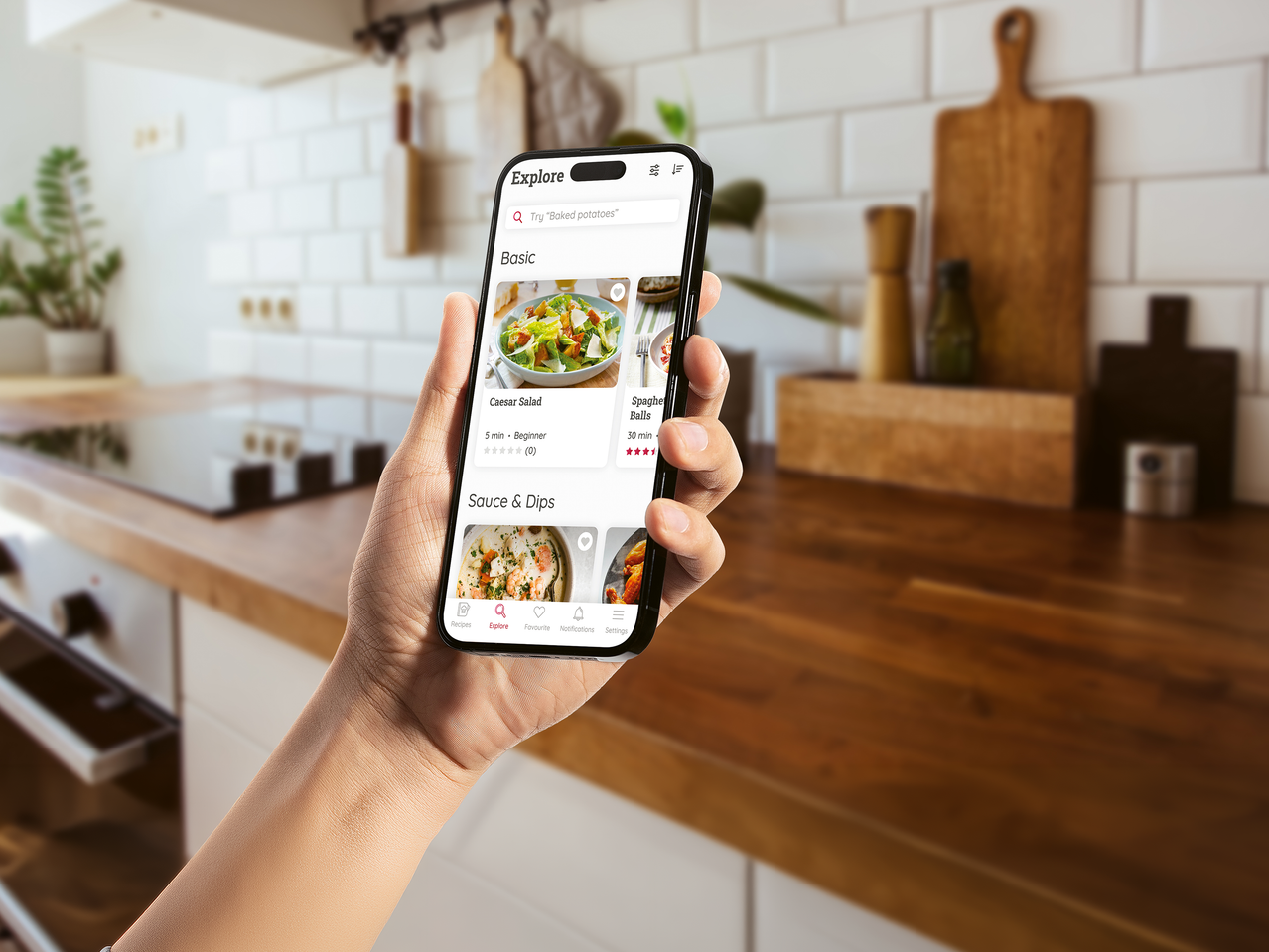 Χέρι κρατάει smartphone που εμφανίζει εφαρμογή συνταγών σε μοντέρνα κουζίνα.