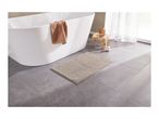A modern bathroom with a white freestanding bathtub, a beige bath mat, and a wooden stool.