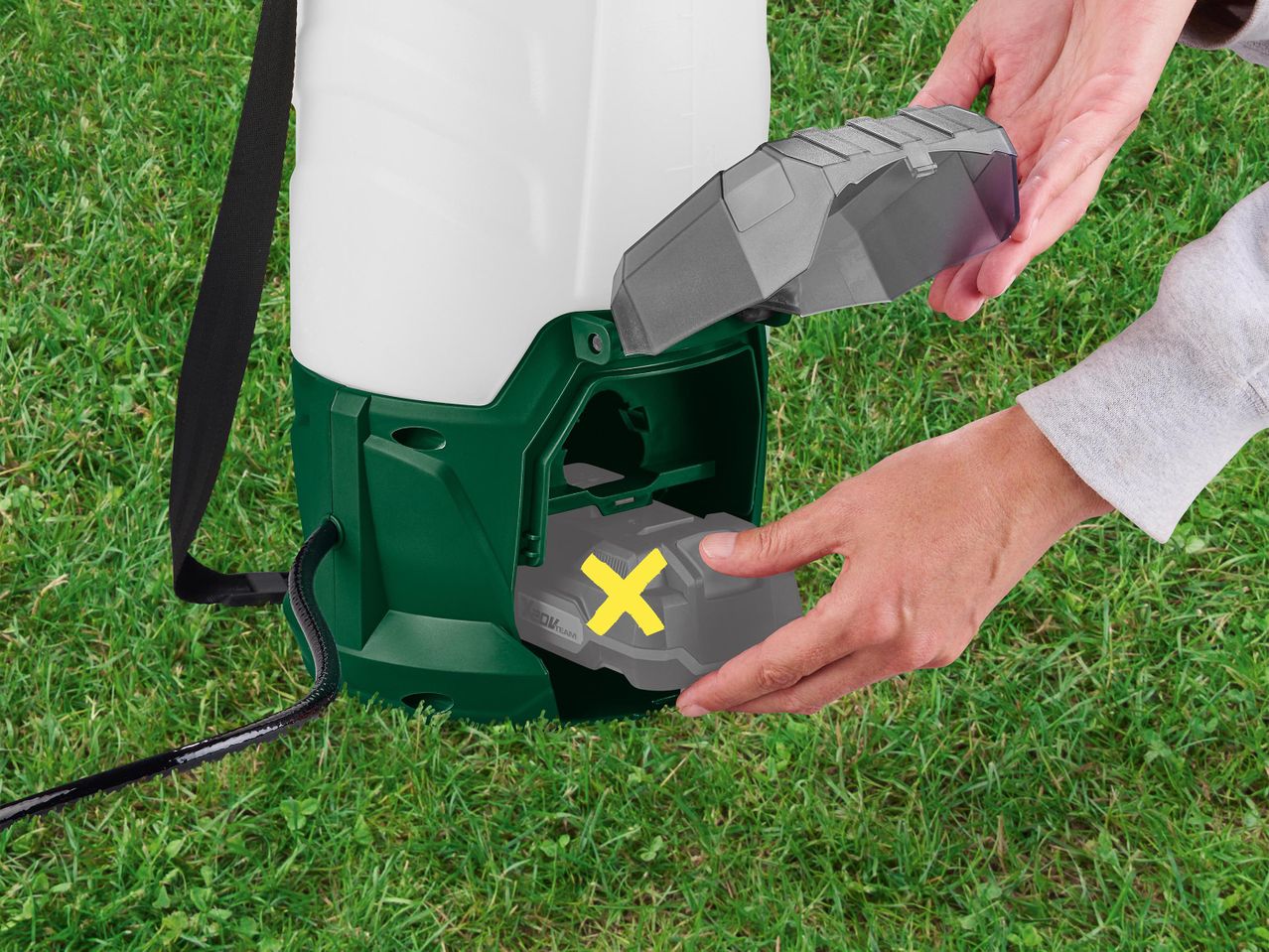 Akkumulátor behelyezése egy zöld-fehér permetezőgépbe, fűben állva.