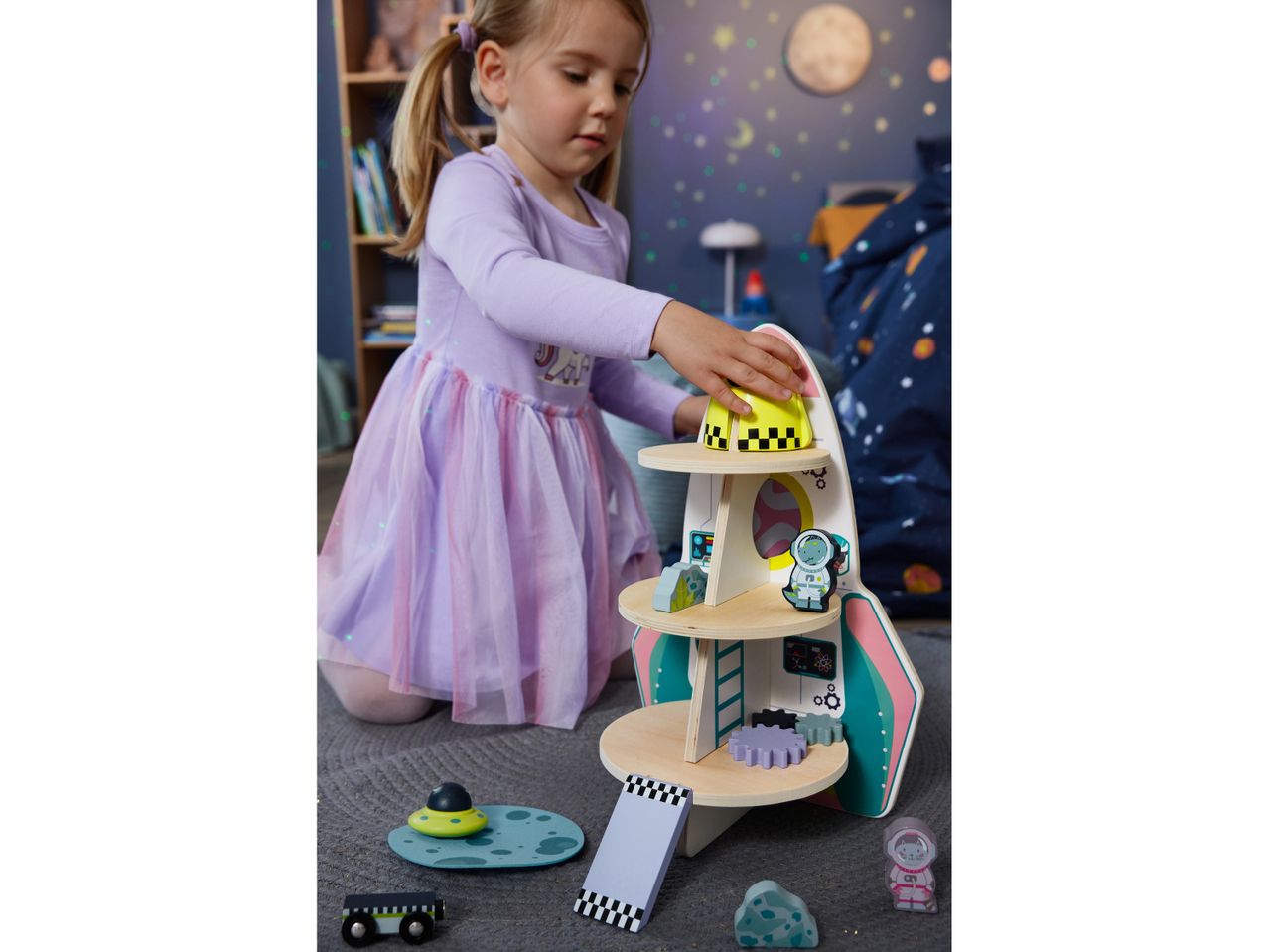 A young girl plays with a Little Dutch wooden rocket ship toy in her space-themed bedroom.