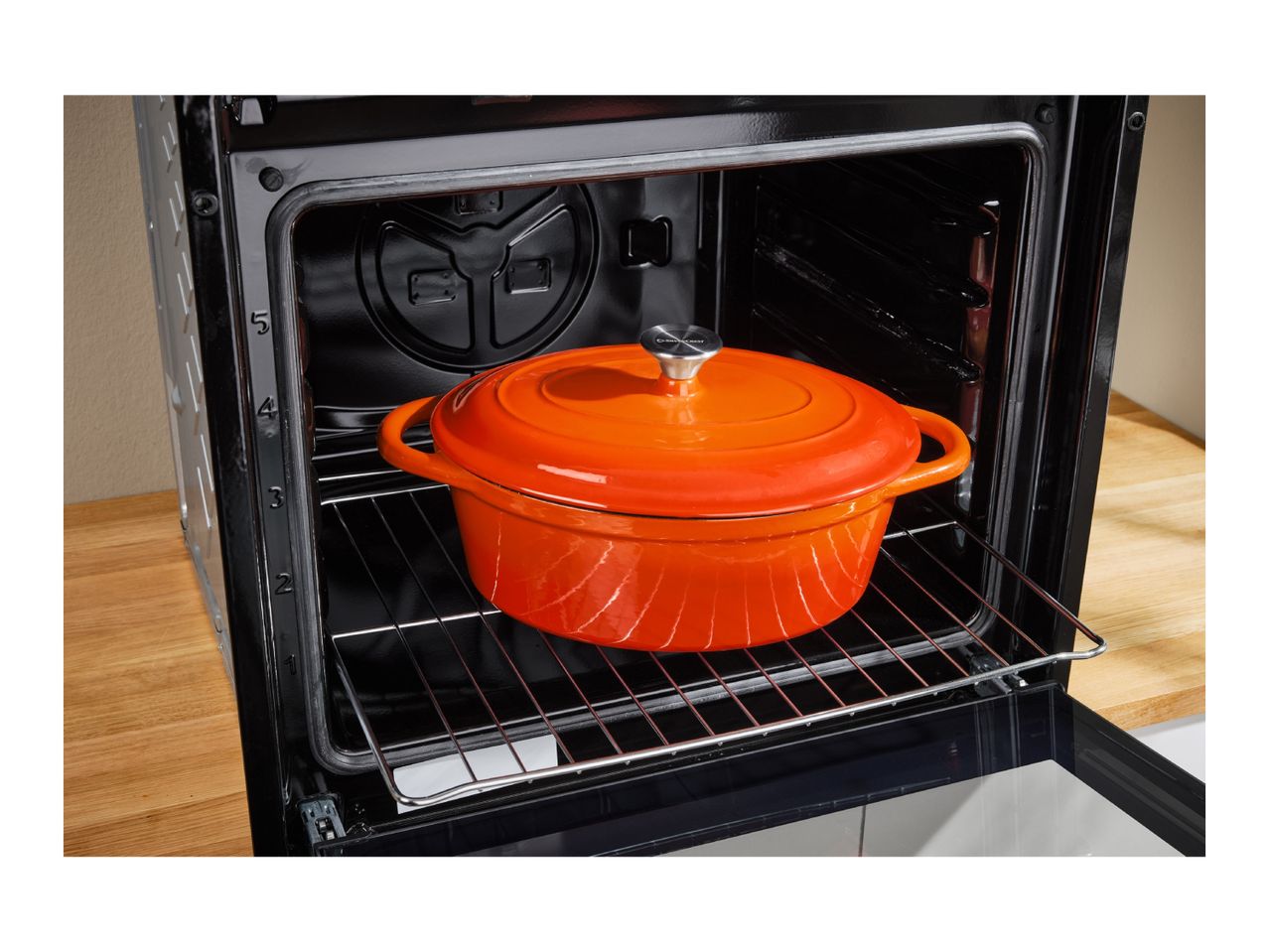 An orange SilverCrest Dutch oven inside a black oven on a metal rack.