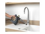 Handheld steam cleaner cleaning a kitchen sink and faucet.
