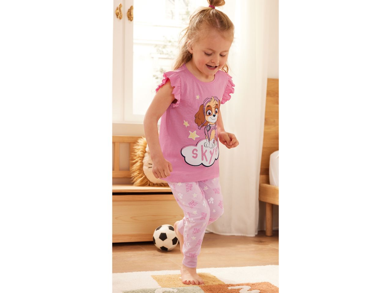 A toddler girl in a pink Paw Patrol Skye pajama set plays in her bedroom.