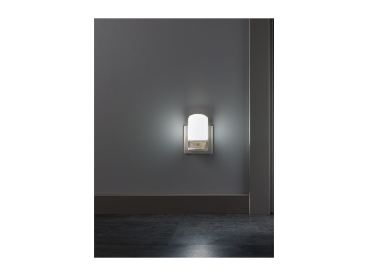 A white night light plugged into a gray wall, illuminating the dark floor.