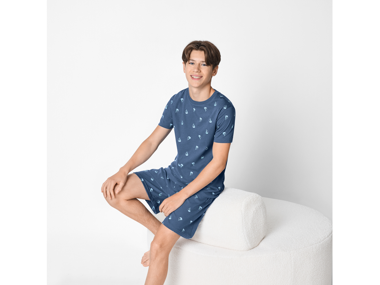 Dječja pidžama ESMARA KIDS u plavoj boji s uzorkom brodova, sjedi na bijeloj klupi.