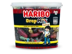 Een grote pot met diverse dropmix, inclusief gekleurde en zwarte drop, met een jongen die snoep vasthoudt.