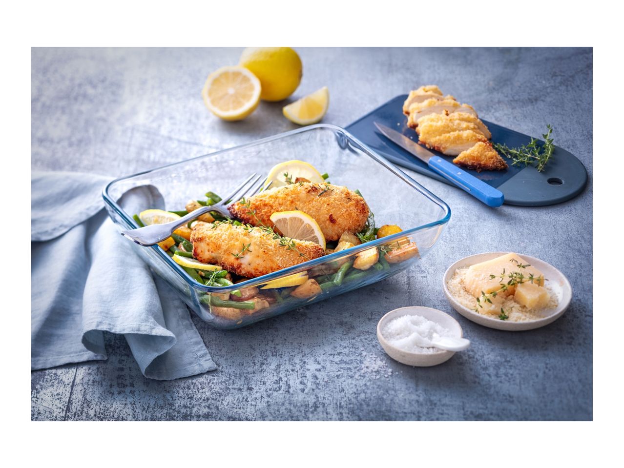 Baked chicken and vegetables in a glass dish with lemons, salt, and cheese.