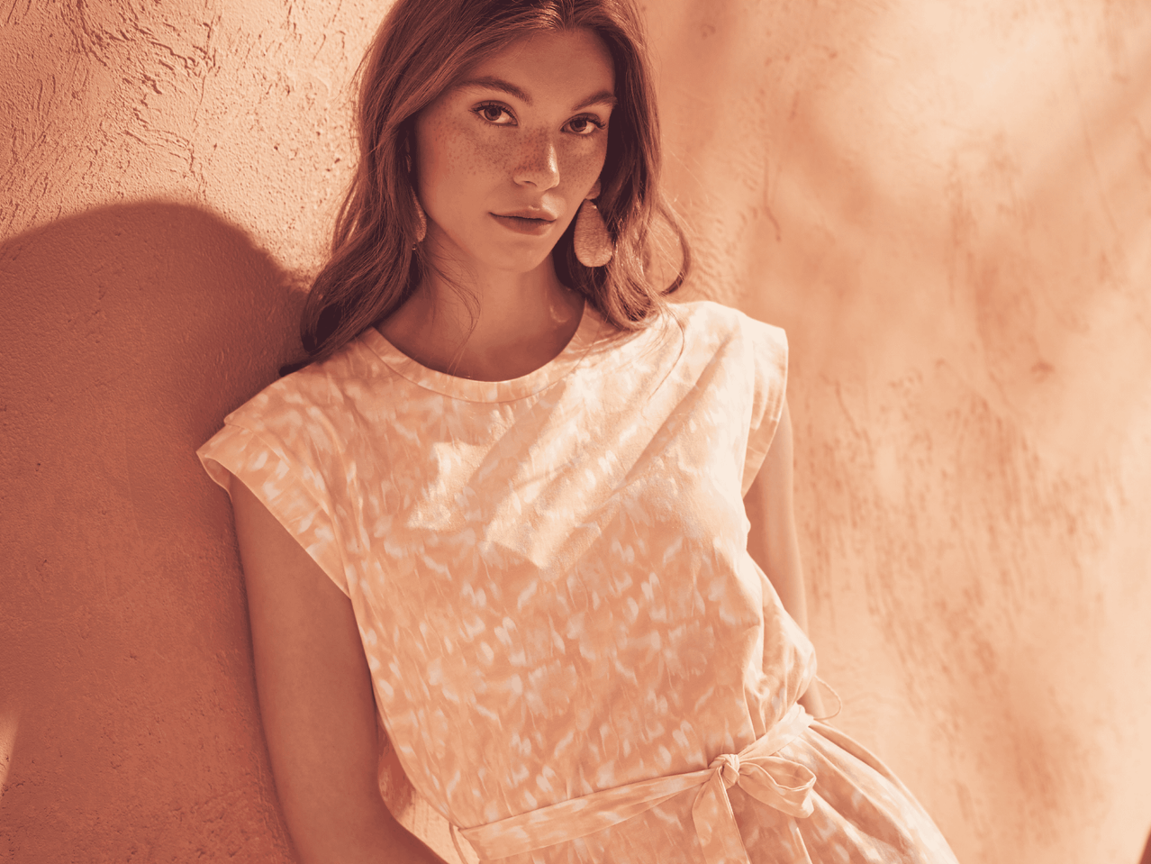 Ein junges Model mit Sommersprossen trägt ein hellbeiges, gemustertes Sommerkleid.