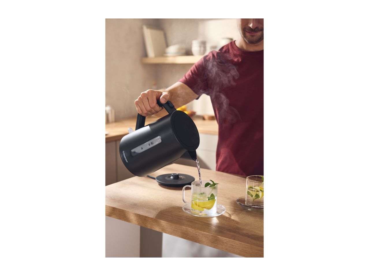 Man pouring hot water from a black kettle into a glass of lemon and mint tea.