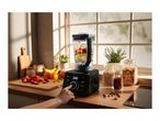 A person using a modern black blender filled with fresh fruit on a kitchen counter.