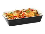 Roasted chicken drumsticks with vegetables and herbs in a black and white baking dish.