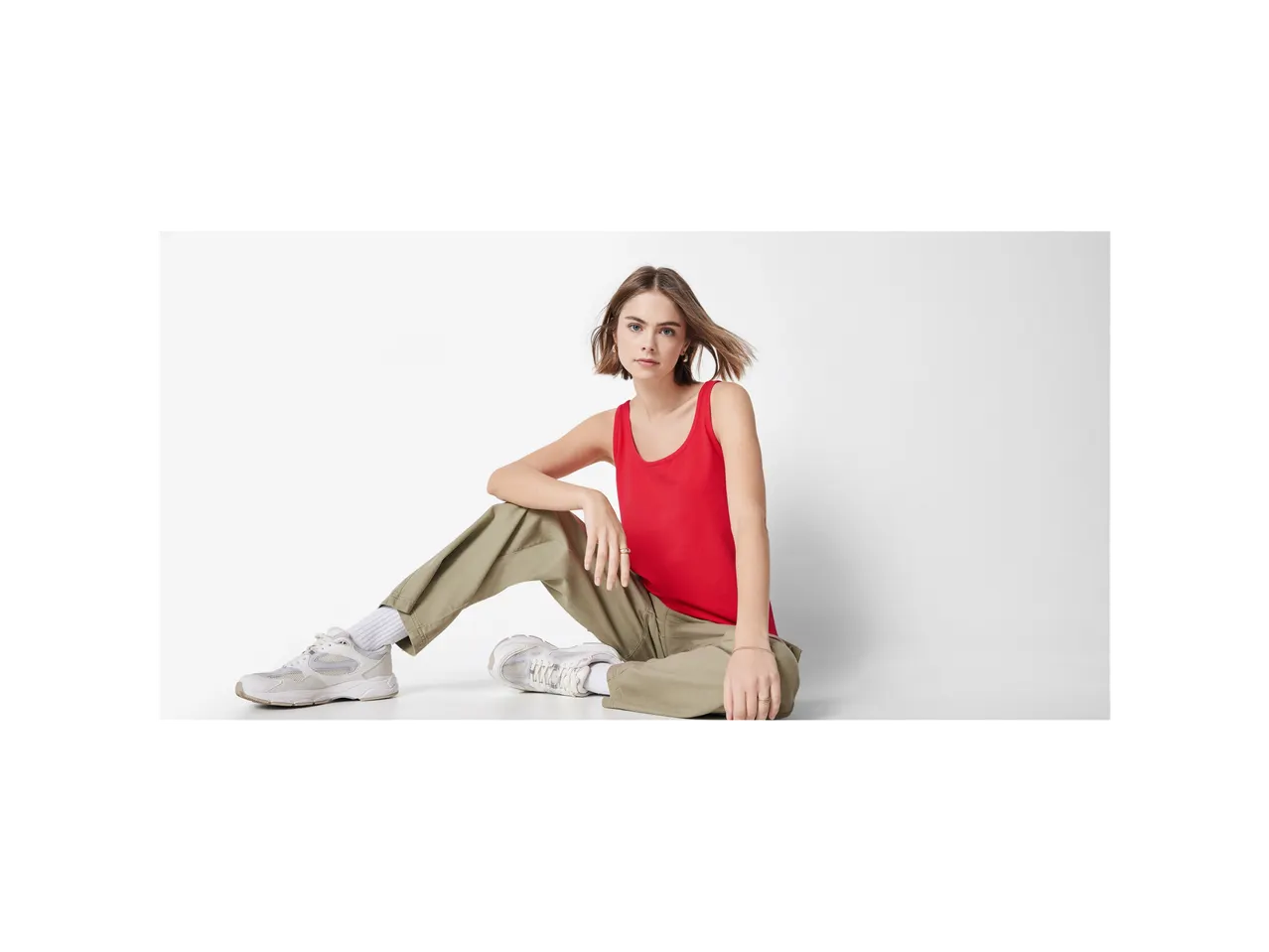 Model în top roșu și pantaloni bej stă pe jos.