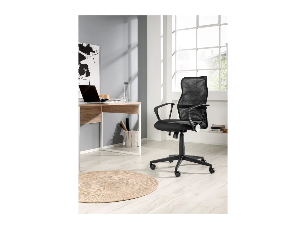 A black mesh office chair in a modern home office with a wooden desk and laptop.