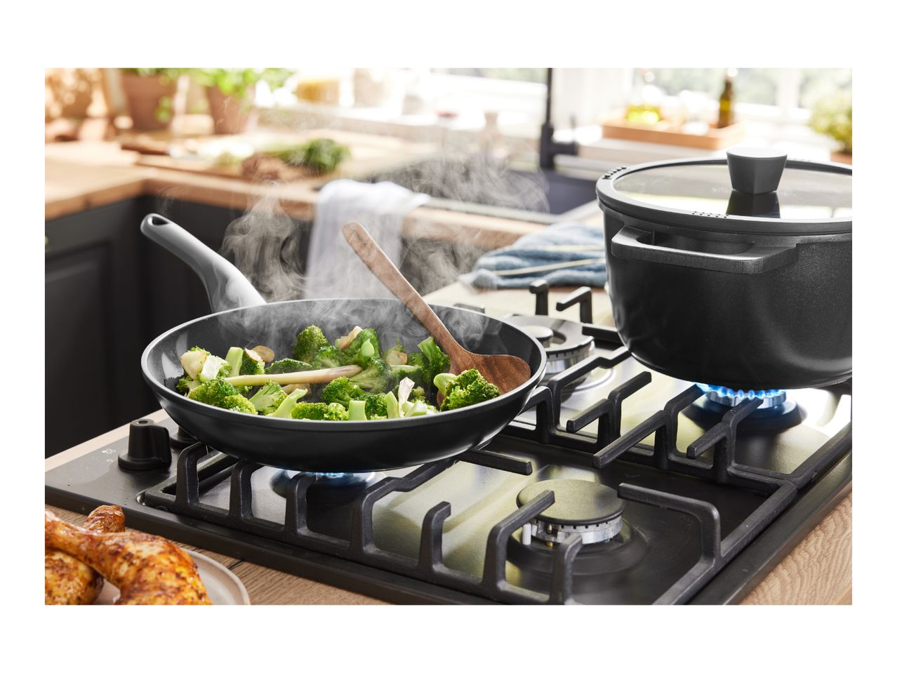A gas stovetop with a frying pan of broccoli and a pot on separate burners.