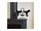 A black dual-blade heat-powered stove fan sitting on top of a wood-burning stove.