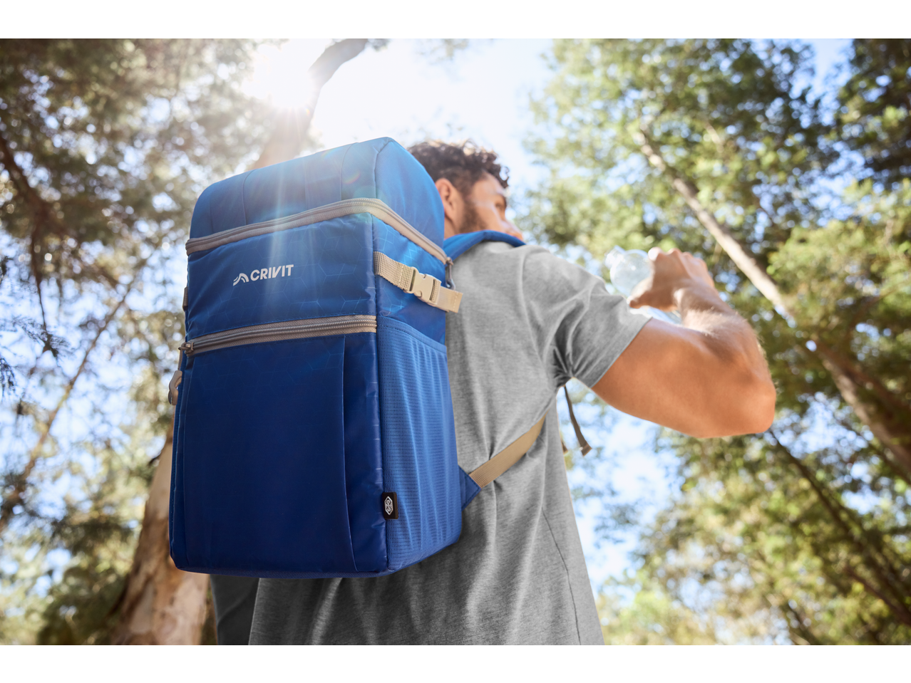 Muškarac sa plavim Crivit rancem pije vodu u šumi.