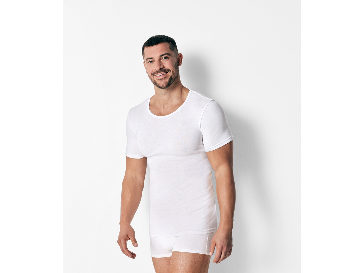 A man smiles while wearing a white undershirt and Calvin Klein underwear.