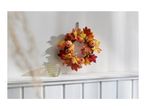 Autumn wreath with pumpkins and leaves, and a glass candle holder on a white shelf.