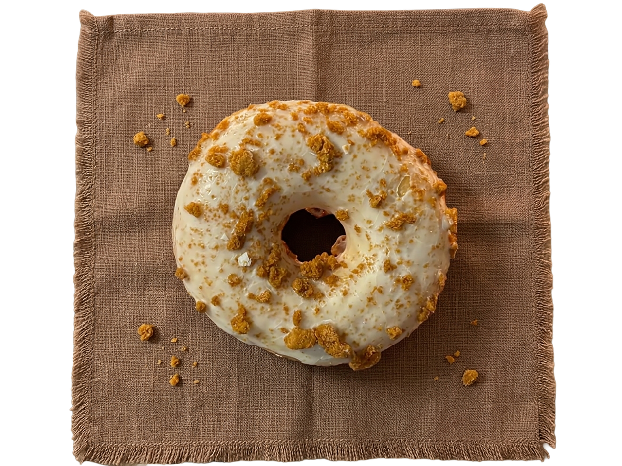 Baltas glazūruotas spurgas su traškiais karamelės gabalėliais ant rudos lininės servetėlės.