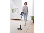 Una donna aspira lo sporco da un tappeto con un aspirapolvere a bastone Grundig.