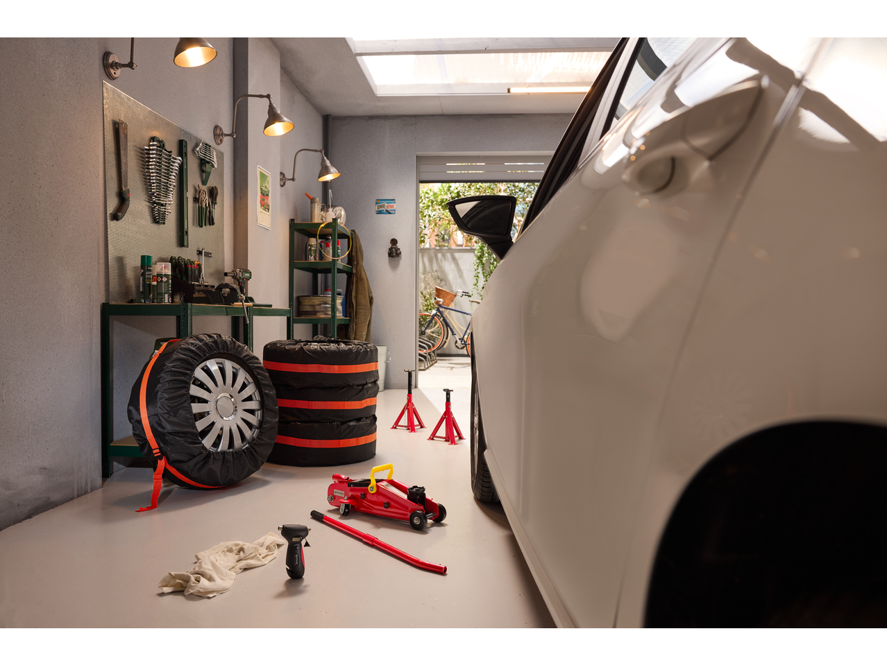 Garage scene with a white car, tyre pressure gauge, car jack, and stacked tyres.