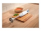 A hand blender on a wooden cutting board next to a bowl of soup