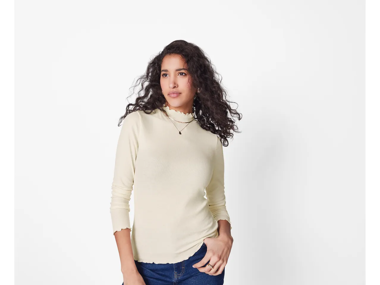 Femeie în bluză esmara bej cu mâneci lungi și blugi albaștri.