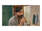 Man in a bathrobe trimming his nose hair with a personal groomer in a bathroom.