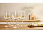 White wine glasses on a wooden counter with cheese, grapes, and breadsticks.