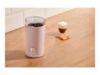 Pink coffee grinder with coffee beans, a glass of coffee, and cookies on a wooden counter.