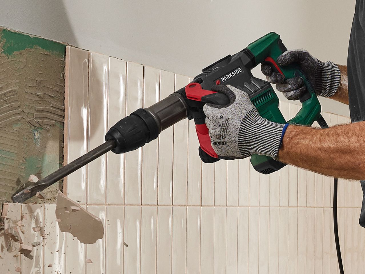 A person uses a Bosch demolition hammer to remove tiles from a wall.