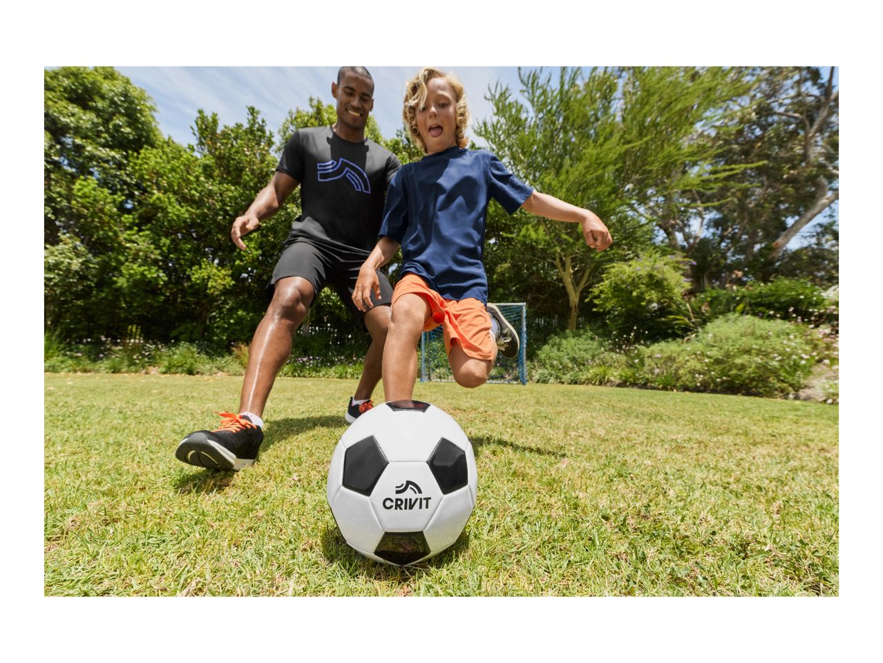 Father and son playing soccer in the garden, with a soccer ball in the foreground.