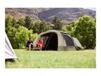 Two people playing cards outside a large camping tent in a grassy area with mountains.