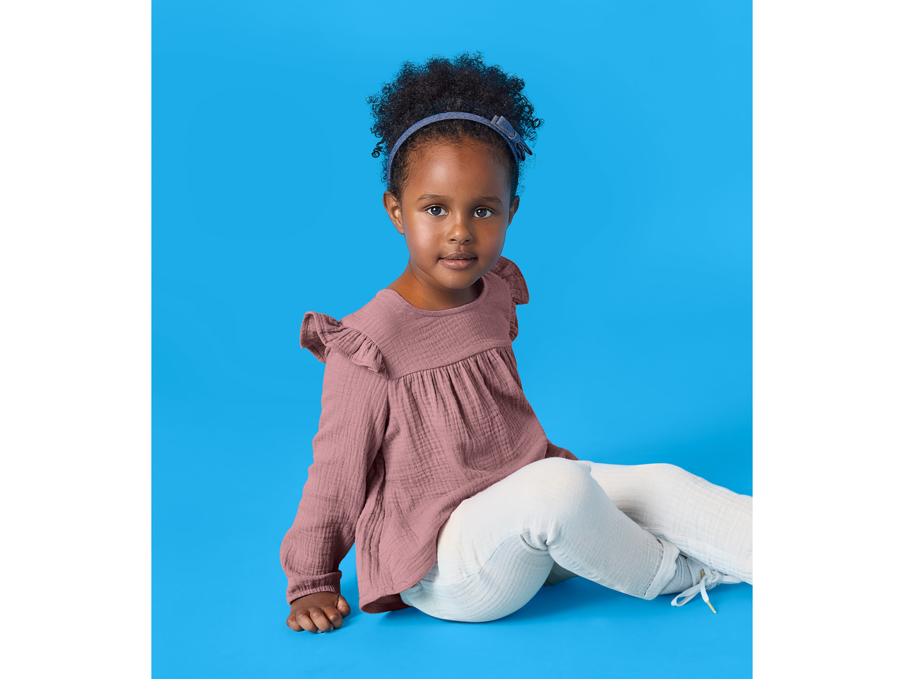 Fetiță purtând bluză de muselină LUPILU și pantaloni albi, așezată.