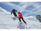 Two skiers, one wearing a red Crivit ski jacket, descend a snowy slope.