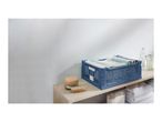 Blue foldable crate with textiles, a brush, and bottles on a wooden shelf.