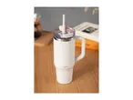 White travel mug with a handle and straw on a wooden table with a book in the background.