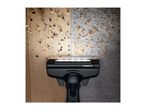 Vacuum cleaner head with LED light on a wooden floor with crumbs and a carpet with lentils.