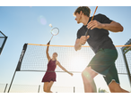Two people playing badminton with a CRIVIT net and rackets under a bright sky.