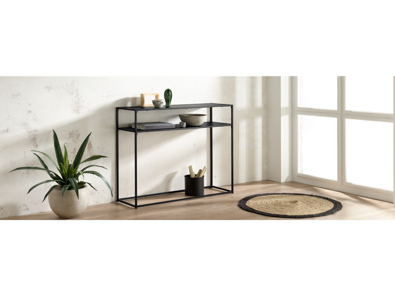 Mesa consola de metal preta Livarno Home com plantas e tapete em uma sala iluminada.