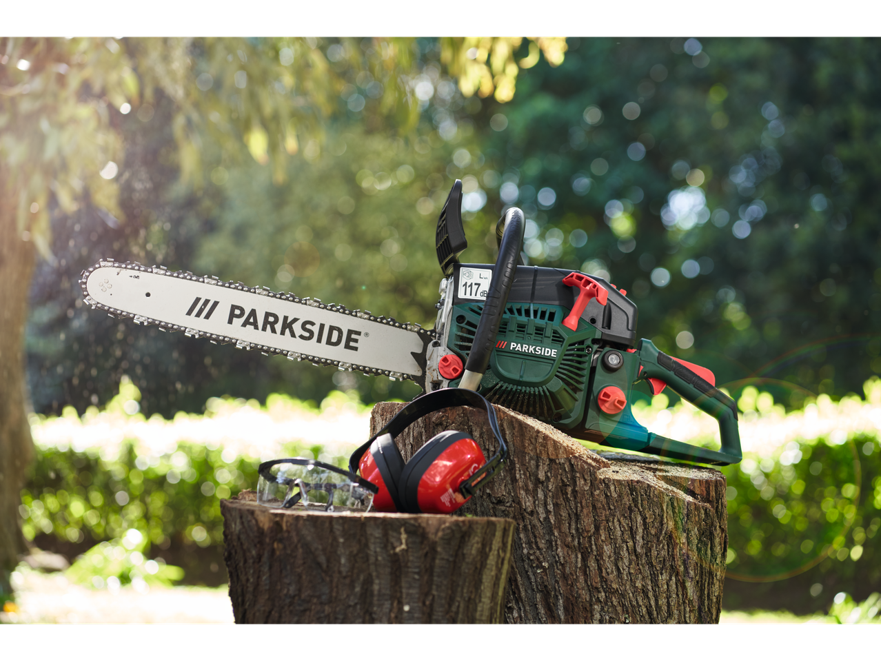 Motosserra Parkside com óculos e protetores auriculares em um toco de árvore.