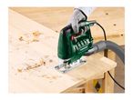Person using a green jigsaw to cut wood, with wood shavings on a wooden workbench.