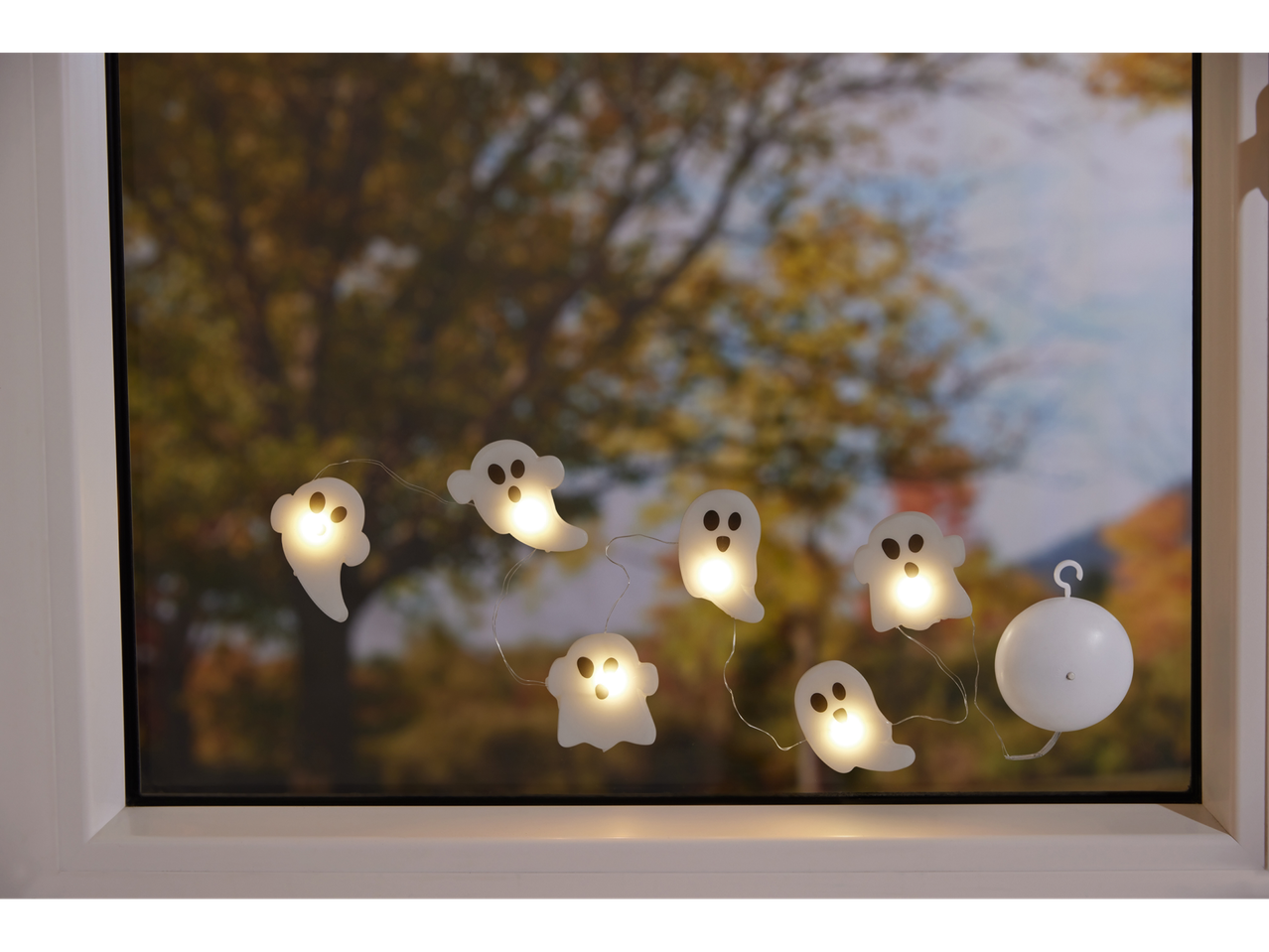 Halloweeni kummituste valguskett aknal, taustal sügispuud