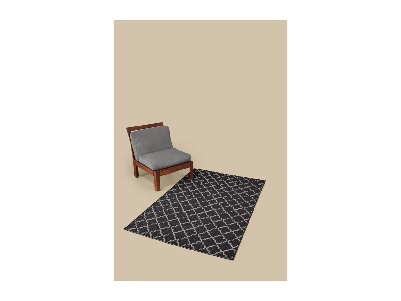 Wooden chair with grey cushions and a black and white patterned rug on a beige background.