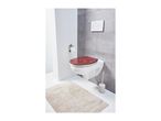 Modern bathroom with a wall-mounted toilet featuring a red patterned seat, a toilet brush, and a beige bath mat.