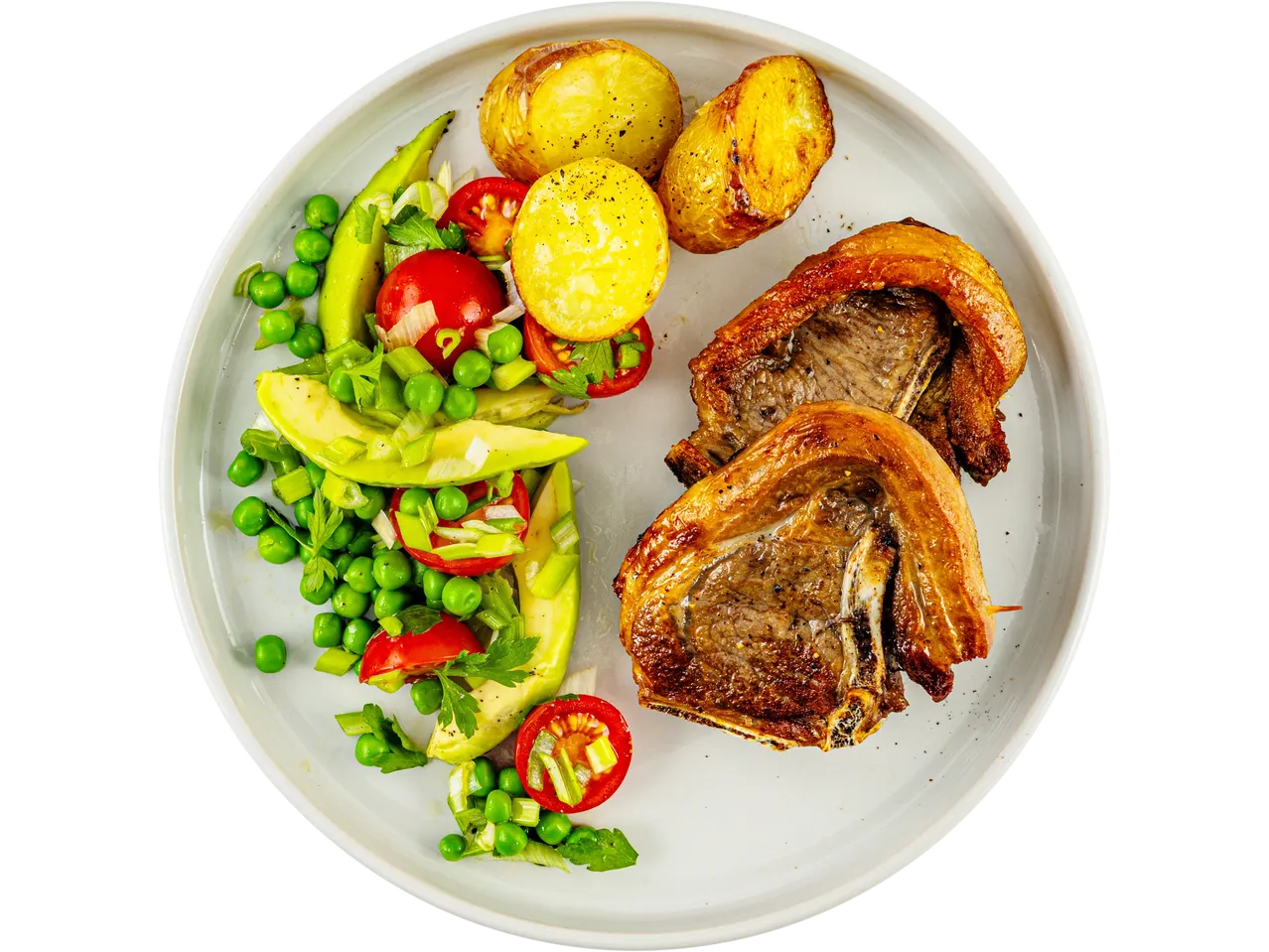 A plate of roasted lamb chops, roasted potatoes, and a fresh pea and avocado salad.