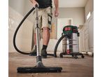A person uses a Bosch wet/dry vacuum cleaner to clean up sawdust on a floor.