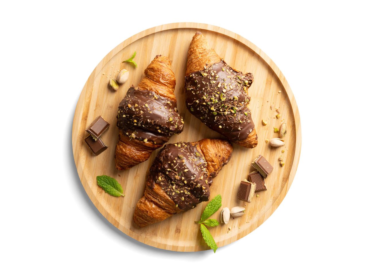 Csokoládéval és pisztáciával szórt croissant-ok egy fa tálcán, menta levelekkel és csokoládé darabokkal.