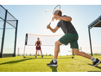 Two people playing badminton with a CRIVIT set on a green court under a clear sky.