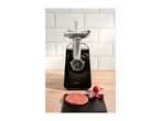 Meat grinder with a raw burger patty and red onions on a wooden surface.
